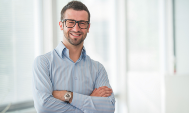 senior account manager con occhiali e bracchia conserte che sorride in camicia azzurra a strisce e sfondo bianco